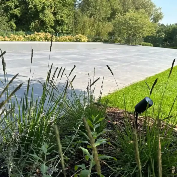 Tamsiai pilkos antracito spalvos Geokeramika Geoceramica lauko plytelės kieme šalia baseino smilgų bei šviestuvo