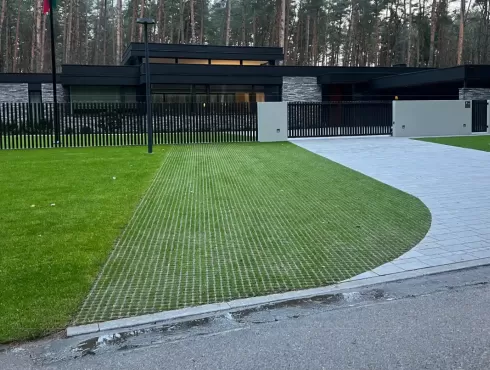 Kvadratinių tinklinių ažūrinių betoninių trinkelių su žaliuojančia veja tvarus ir estetiškas grindinys moderniame kieme 
